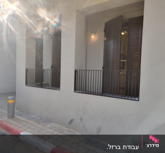 חלונות עם תריסים חומים ומעקה מתכת שחור